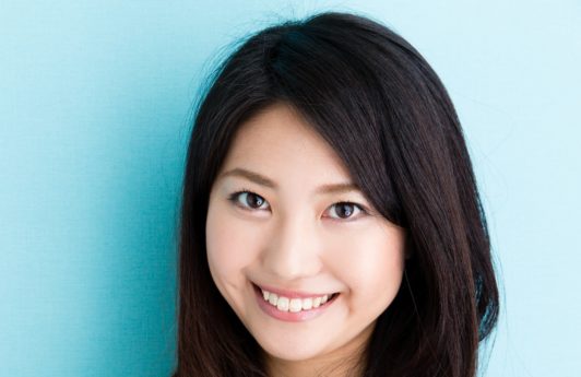 Best haircuts for long hair: Asian woman with long black wavy hair close up shot against a blue background