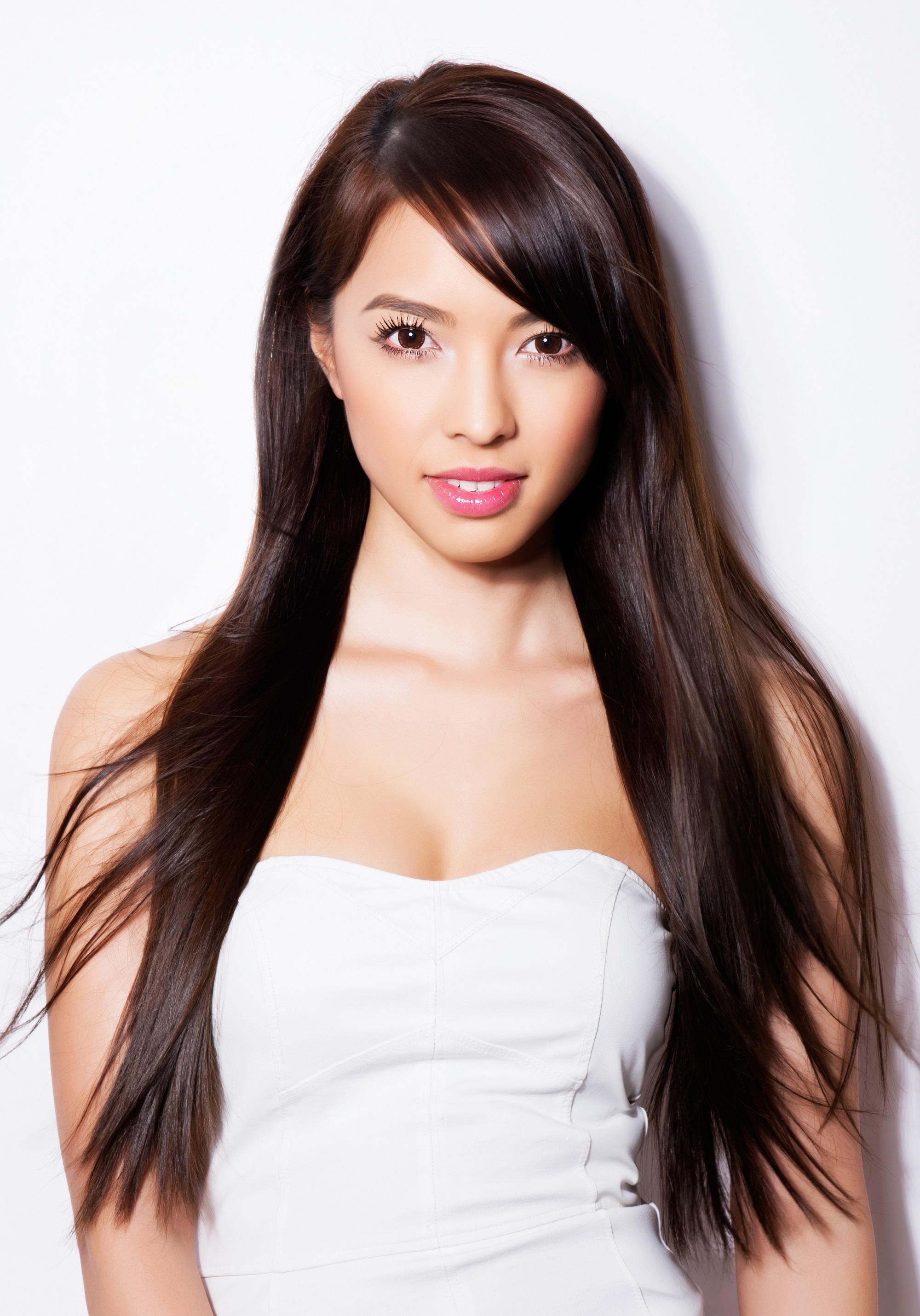 Meilleures coupes de cheveux pour cheveux longs : Femme portant un haut tube blanc avec de longs cheveux noirs et une frange latérale debout sur fond blanc