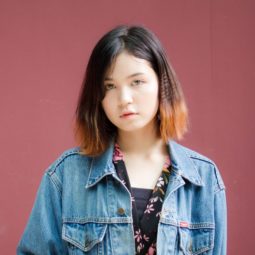 Blunt haircut: Girl wearing a denim jacket with blunt bob dip dyed brown standing against a burgundy background