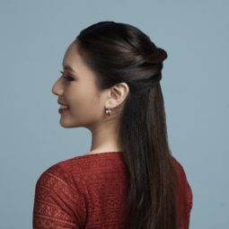 Half up criss cross: Side view of an Asian woman wearing a red dress with long black hair in half up criss cross hairstyle standing against a blue background