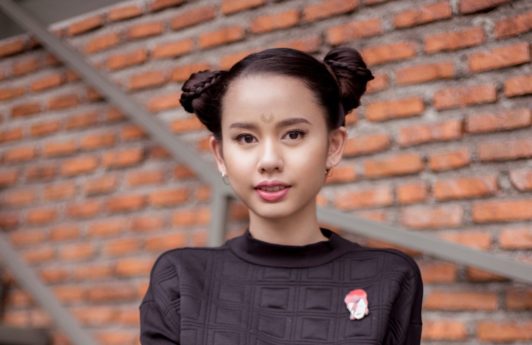 Asian girl with hair in Halloween glam double buns in outdoor location against a brick wall