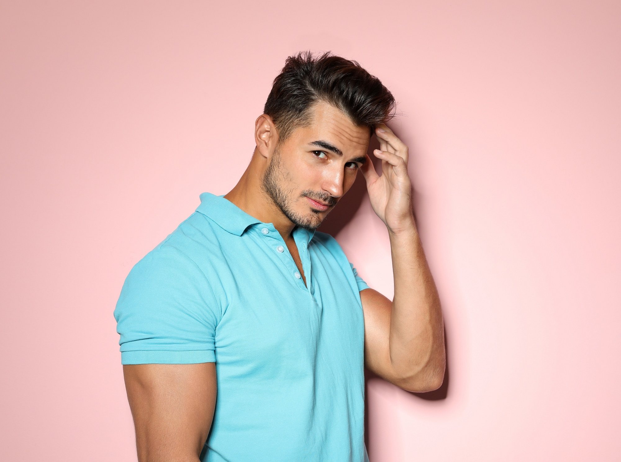 Shaved side hairstyles men: Main wearing a blue polo shirt touching his hair and standing against a pink background