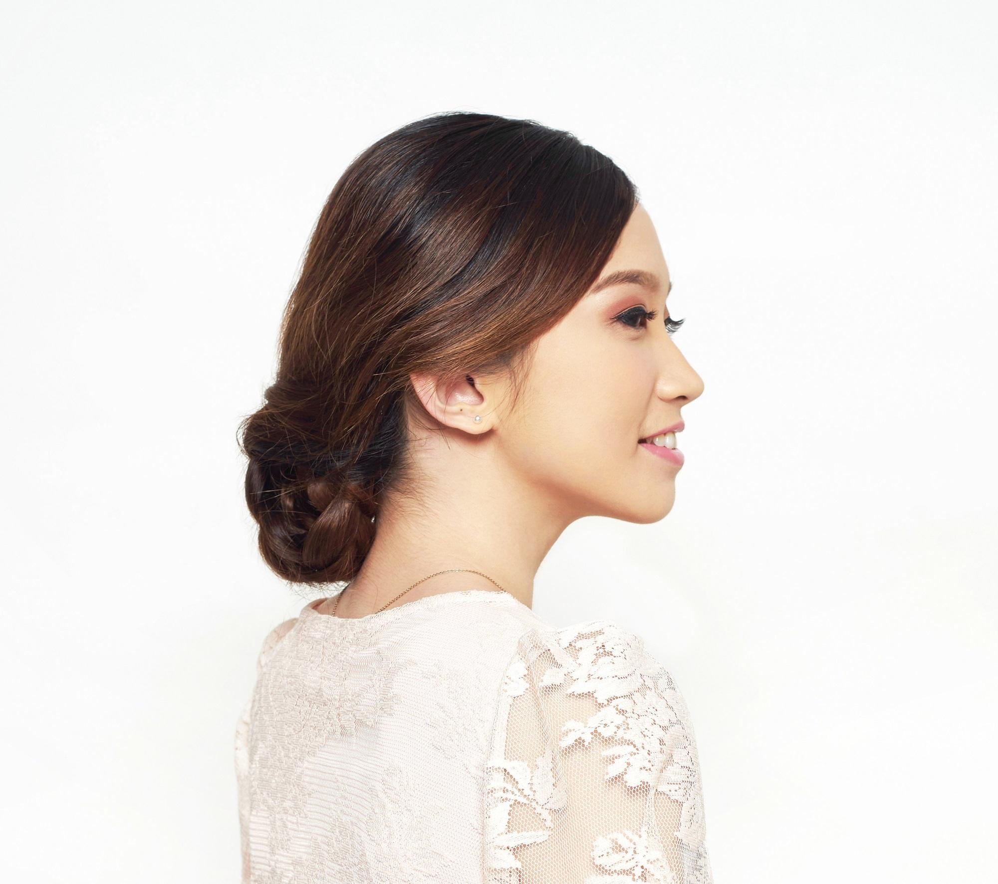 Wedding hairstyles for medium hair: Asian woman wearing light pink dress with dark brown hair in braided updo against a white background
