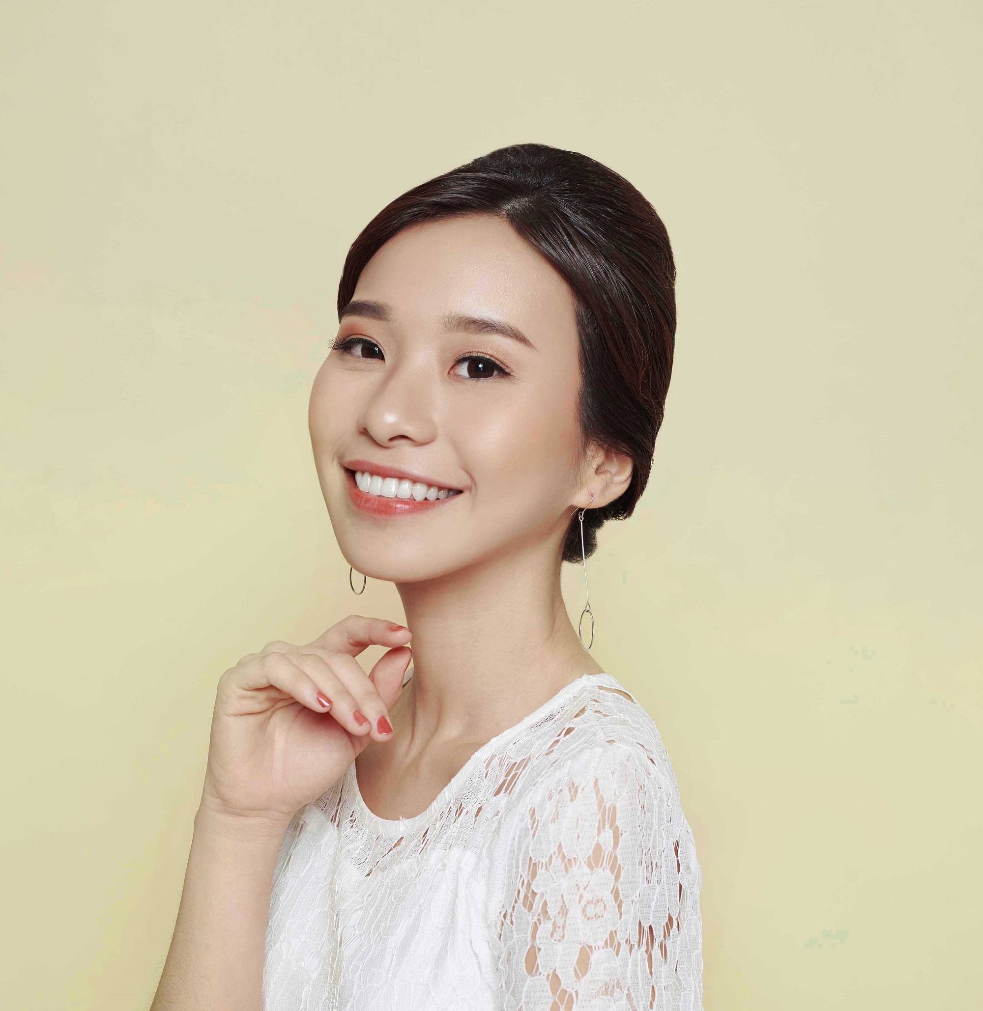 Wedding hairstyles for medium hair: Closeup shot of Asian woman in white dress with hair in French twist against a champagne-colored background