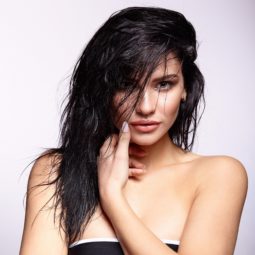 Wet hair look: Closeup shot of a woman with long messy black hair wearing a black tube top against a white background
