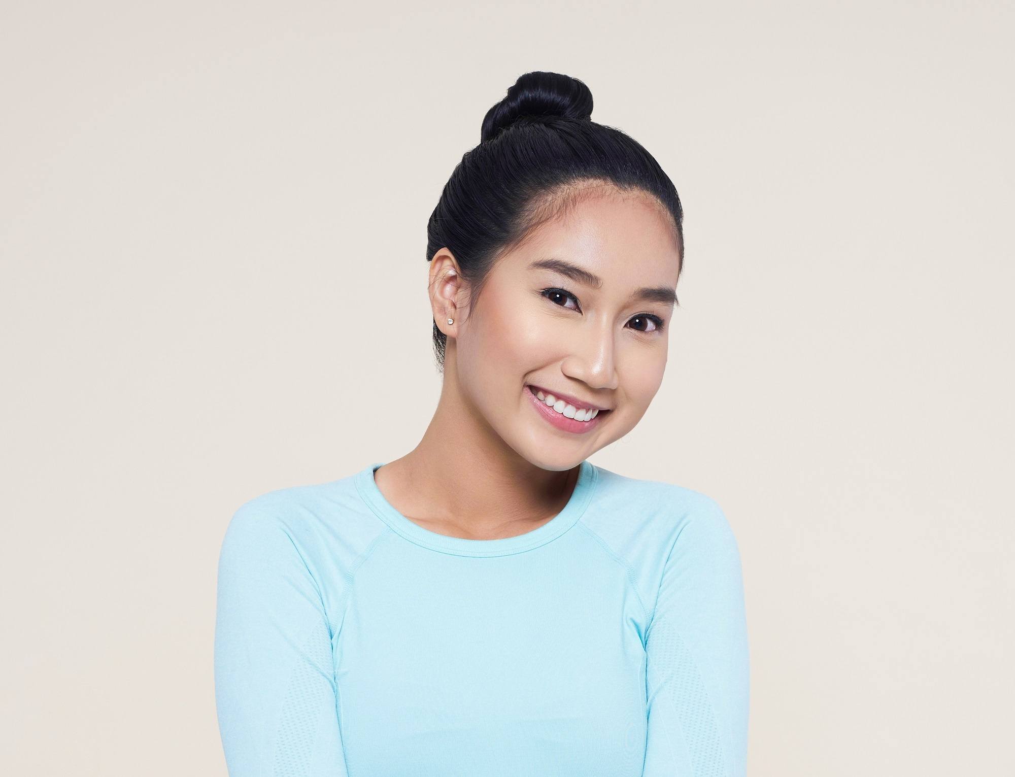 Advent calendar: Closeup shot of an Asian woman with long black hair in a bun wearing light blue shit against an oyster-colored background