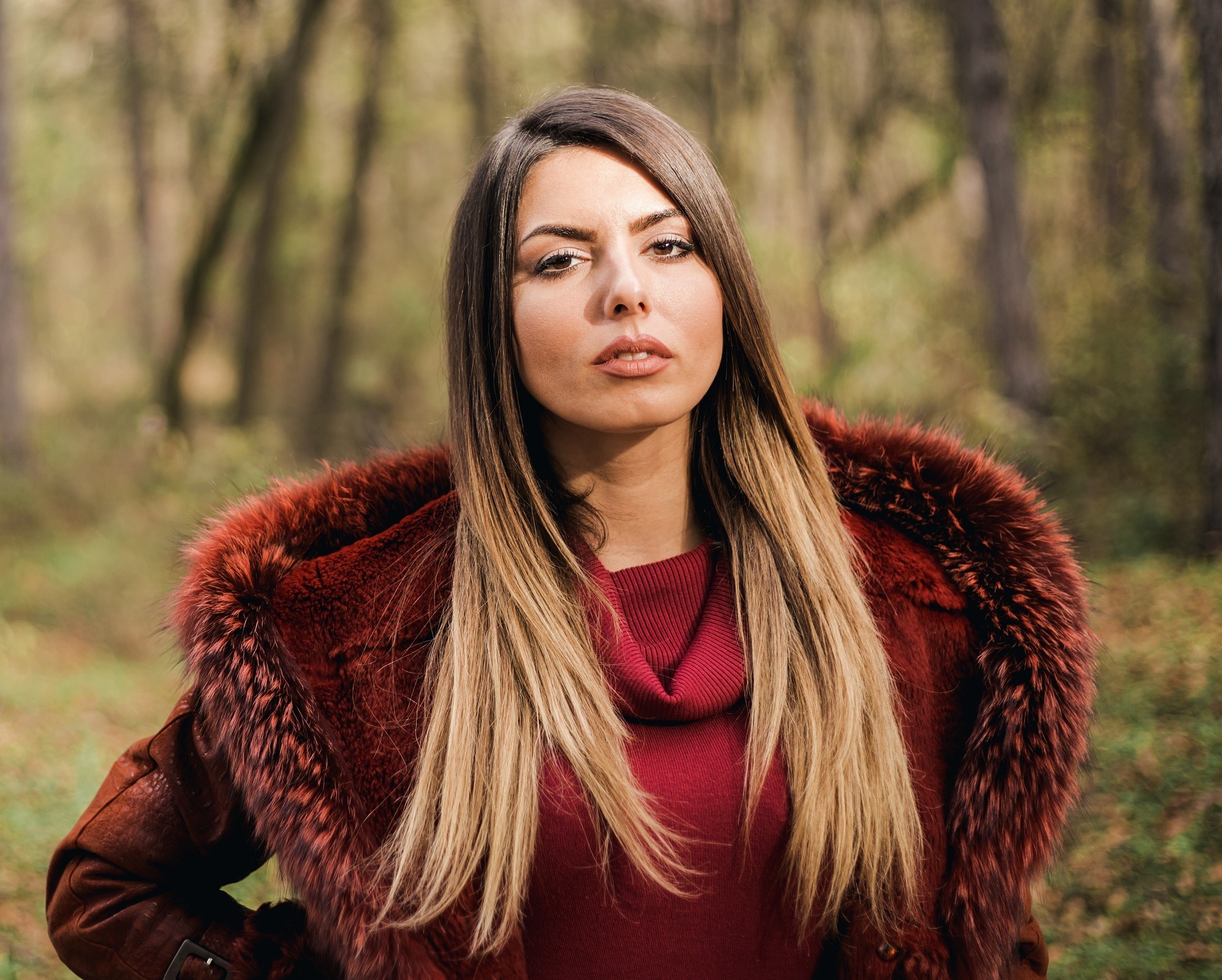 Brown ombre hair: Woman with ash brown and blonde hair wearing a red coat in a forest
