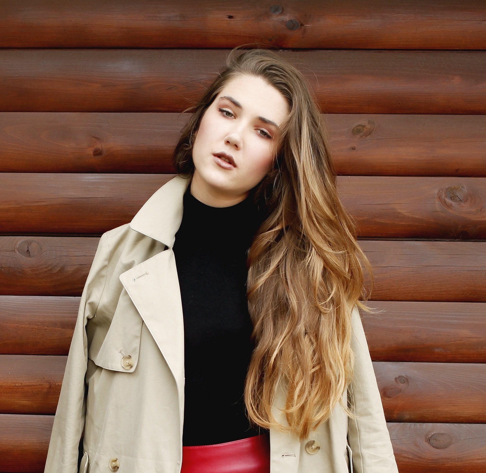 Brown ombre hair: Woman wearing a black top and red skirt and cream-colored coat with bronde wavy hair
