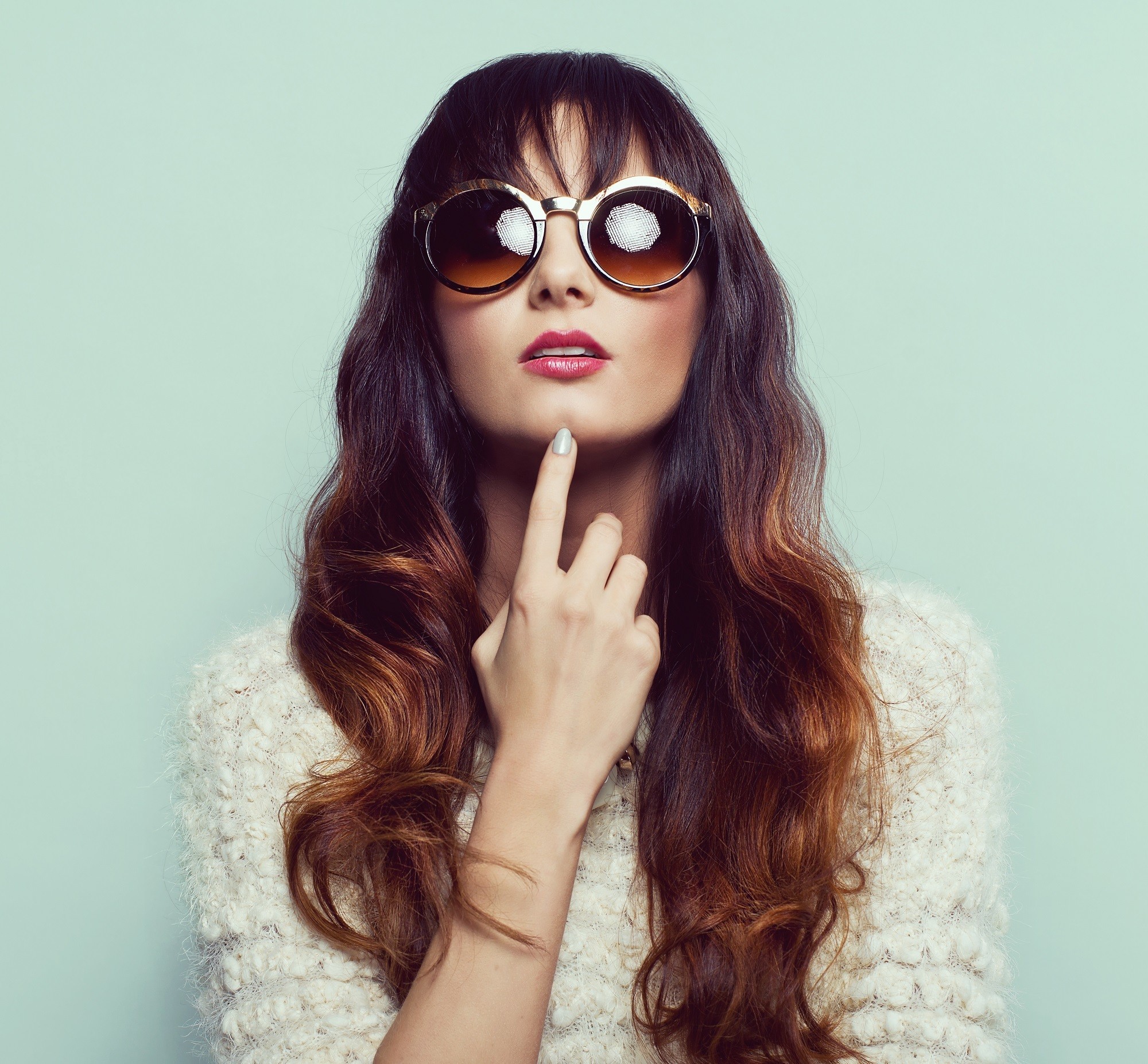 Brown ombre hair: Woman wearing a while blouse and shades with long brown wavy hair with bangs