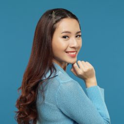 Curly side part hairstyle Asian woman with long dark brown hair with hair clips wearing a blue cardigan against a blue background