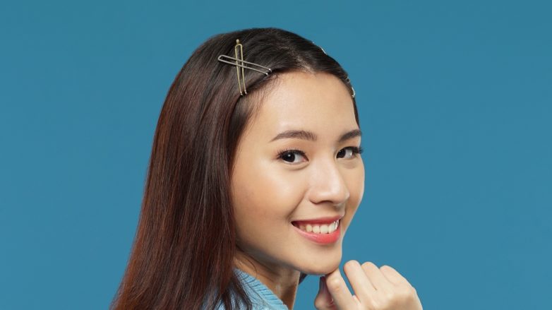 Curly side part hairstyle Asian woman with long dark brown hair with hair clips wearing a blue cardigan against a blue background