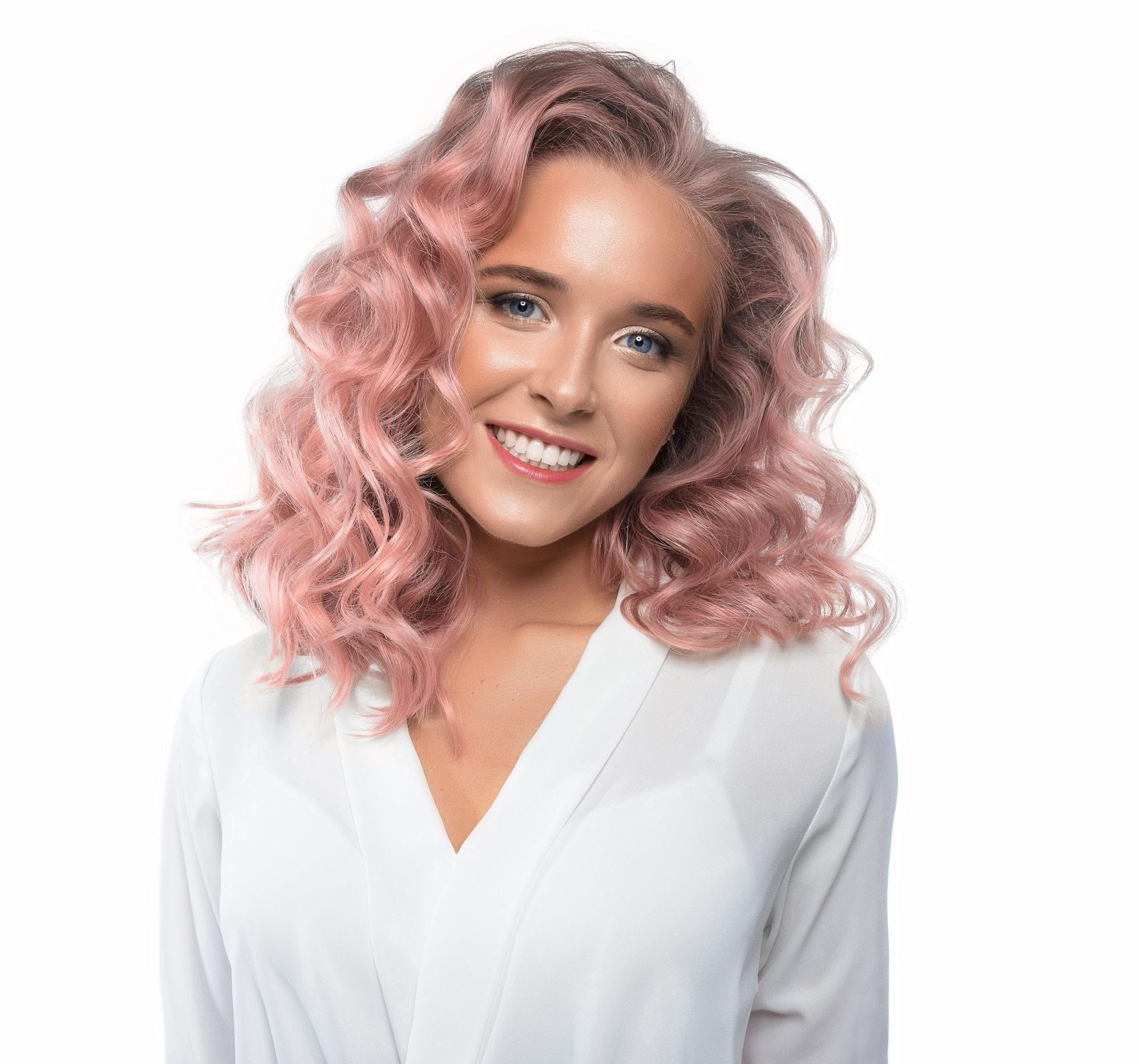 Hair color for curly hair: Closeup shot of a woman with pink shoulder-length curly hair wearing white top against white background