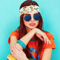 Hippie hairstyles: Closeup shot of woman with long hair and printed headband and wearing an orange shirt against a blue background