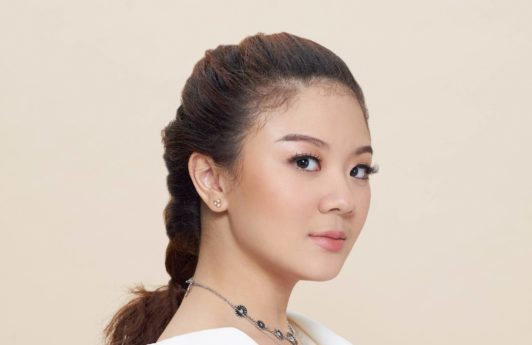 Pull through braid: Closeup shot of Asian woman wearing white blouse with brown hair in pull through braid standing against oyster-colored background
