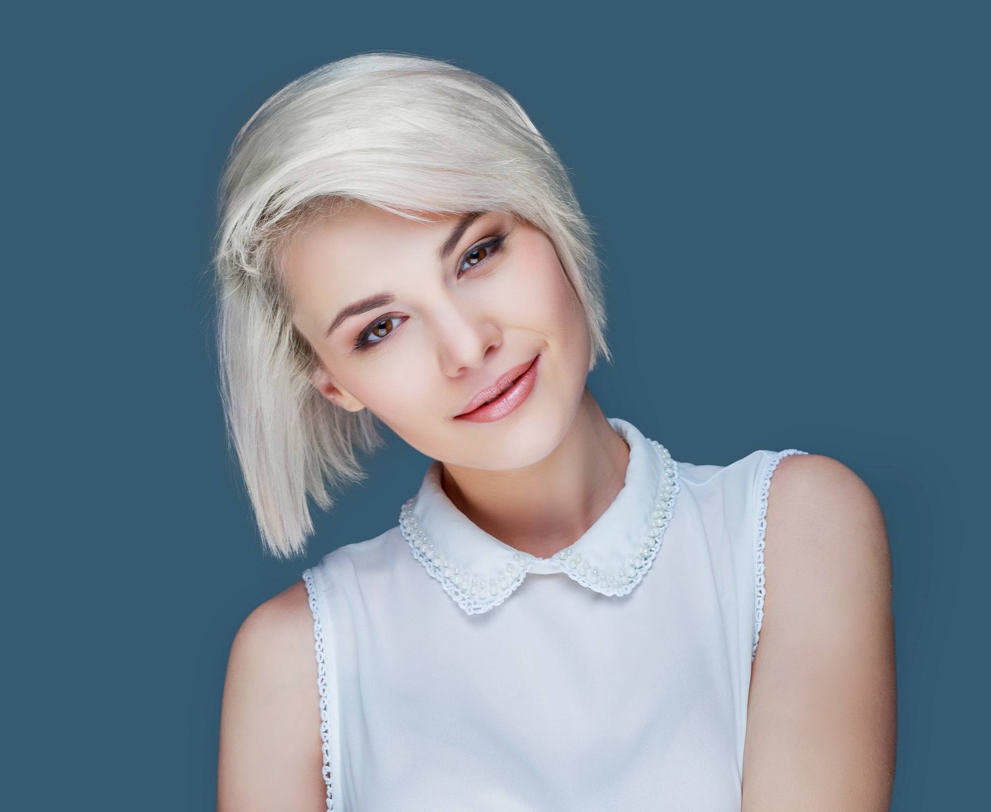 Short blonde hair: Closeup shot of a woman with short blonde hair wearing a white sleeveless top against a blue background