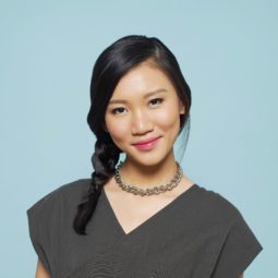 Side part hairstyles: Closeup shot of Asian woman with long black hair in side braid wearing gray blouse against a blue background