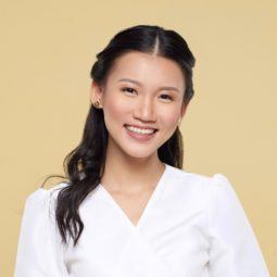 Twisted ponytail half updo: Closeup shot of an Asian woman with long black hair wearing a white blouse against a yellow background