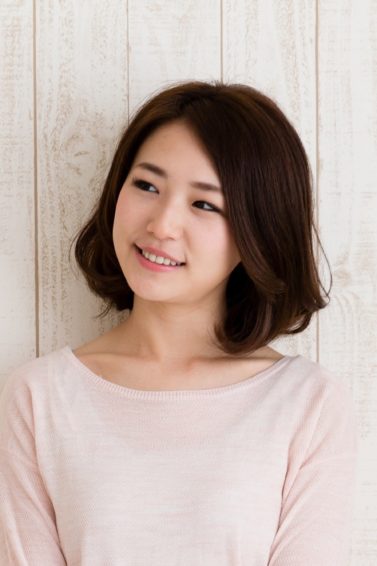 Best haircuts for different face shapes: Closeup shot of an Asian woman with dark lob wearing a light pink sweater