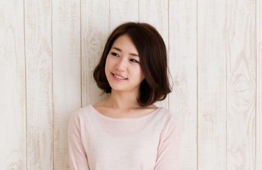 Best haircuts for different face shapes: Closeup shot of an Asian woman with dark lob wearing a light pink sweater