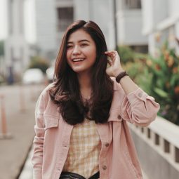 Asian woman with long layered brown hair wearing a pink jacket outdoors