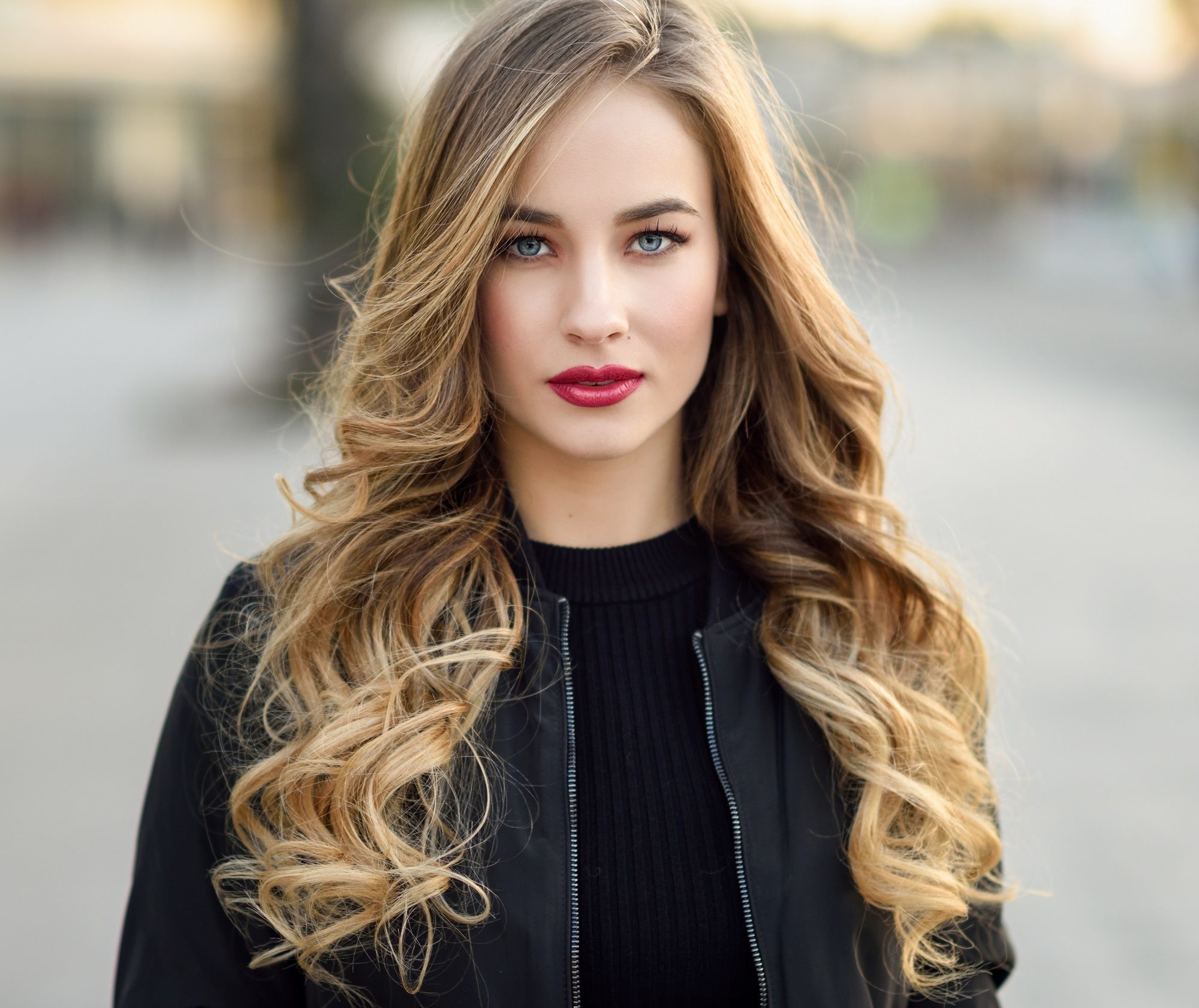 Curly blonde hair: Closeup shot of a woman with long bronde curly hair wearing black long sleeved-top outdoors