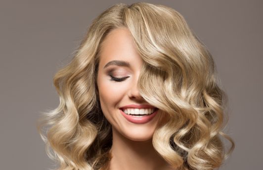 Curly blonde hair: Closeup shot of Caucasian woman with curly blonde hair against a gray background