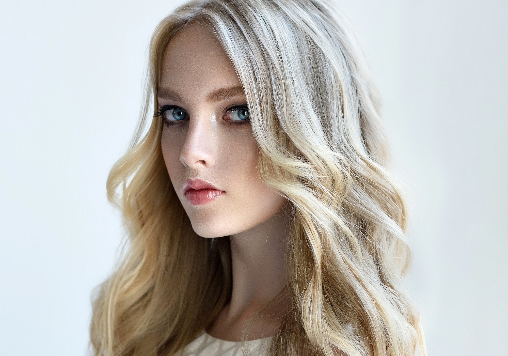 Curly blonde hair: Closeup shot of Caucasian woman with long wavy sandy blonde hair against a white background