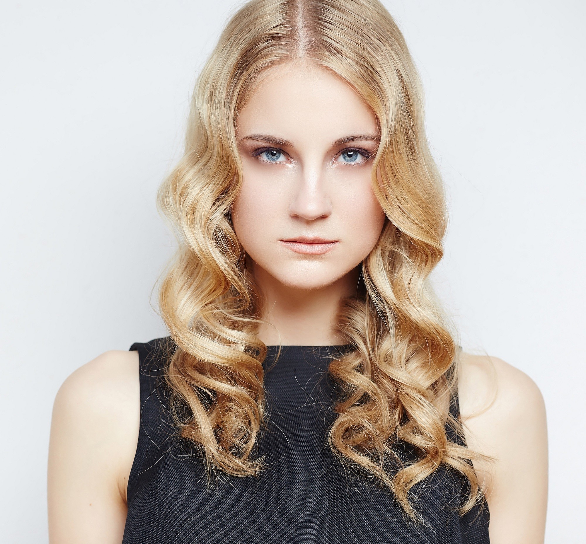 Curly blonde hair: Closeup shot of Caucasian woman with long curly strawberry blonde hair wearing black sleeveless top against a white background