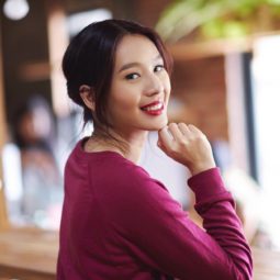 Get the look holiday hairstyles: Closeup shot of an Asian woman with black hair in a banana bun wearing fuchsia sweater in a cafe