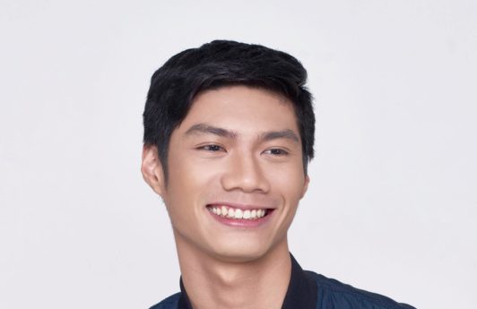 How to style short hair for men: Closeup shot of Asian man with short black hair smiling wearing a blue jacket and white shirt