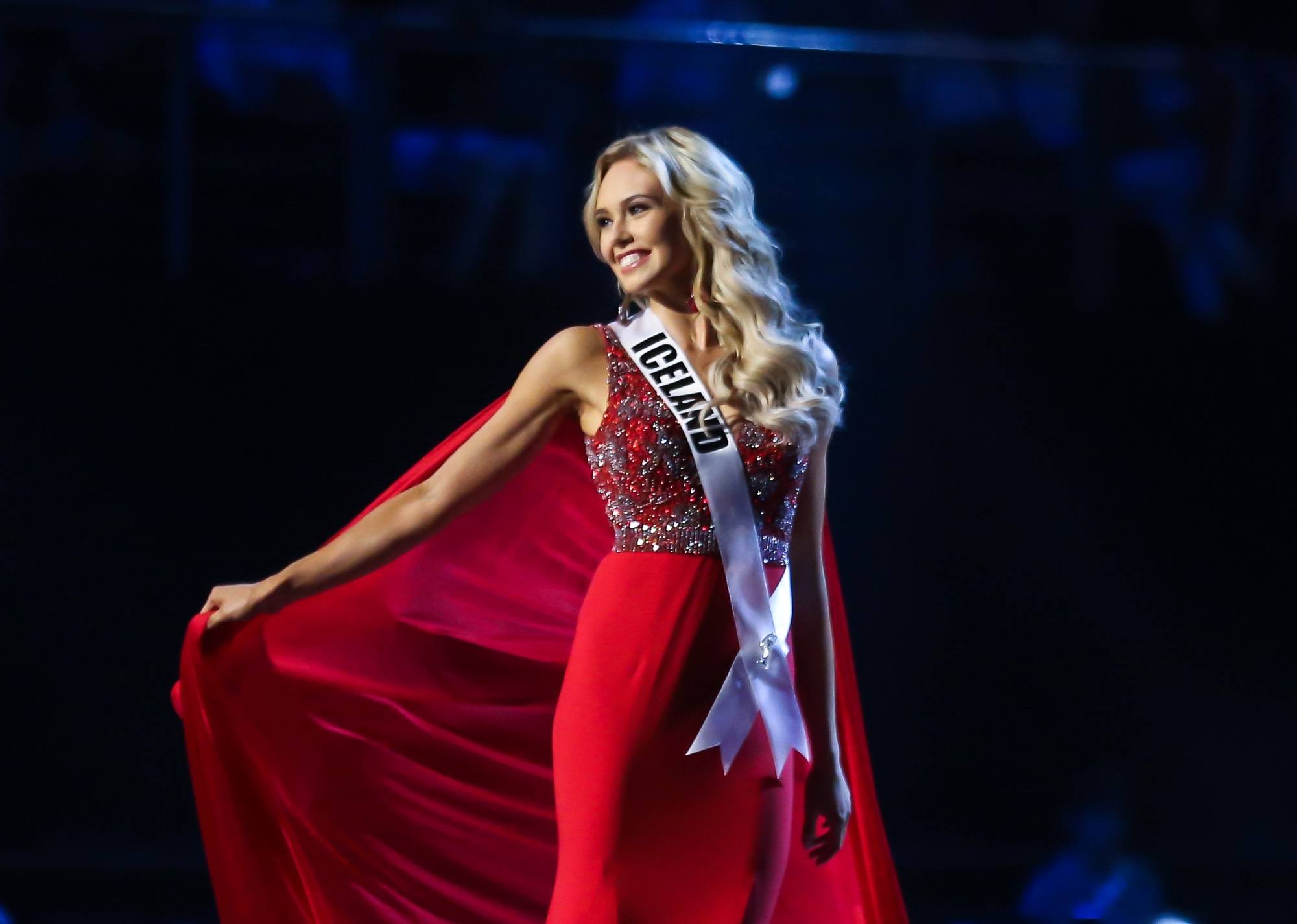Miss Universe 2018 hairstyles: Miss Iceland Katrin Lea Elenudottir with long blonde wavy hair wearing a red gown on stage