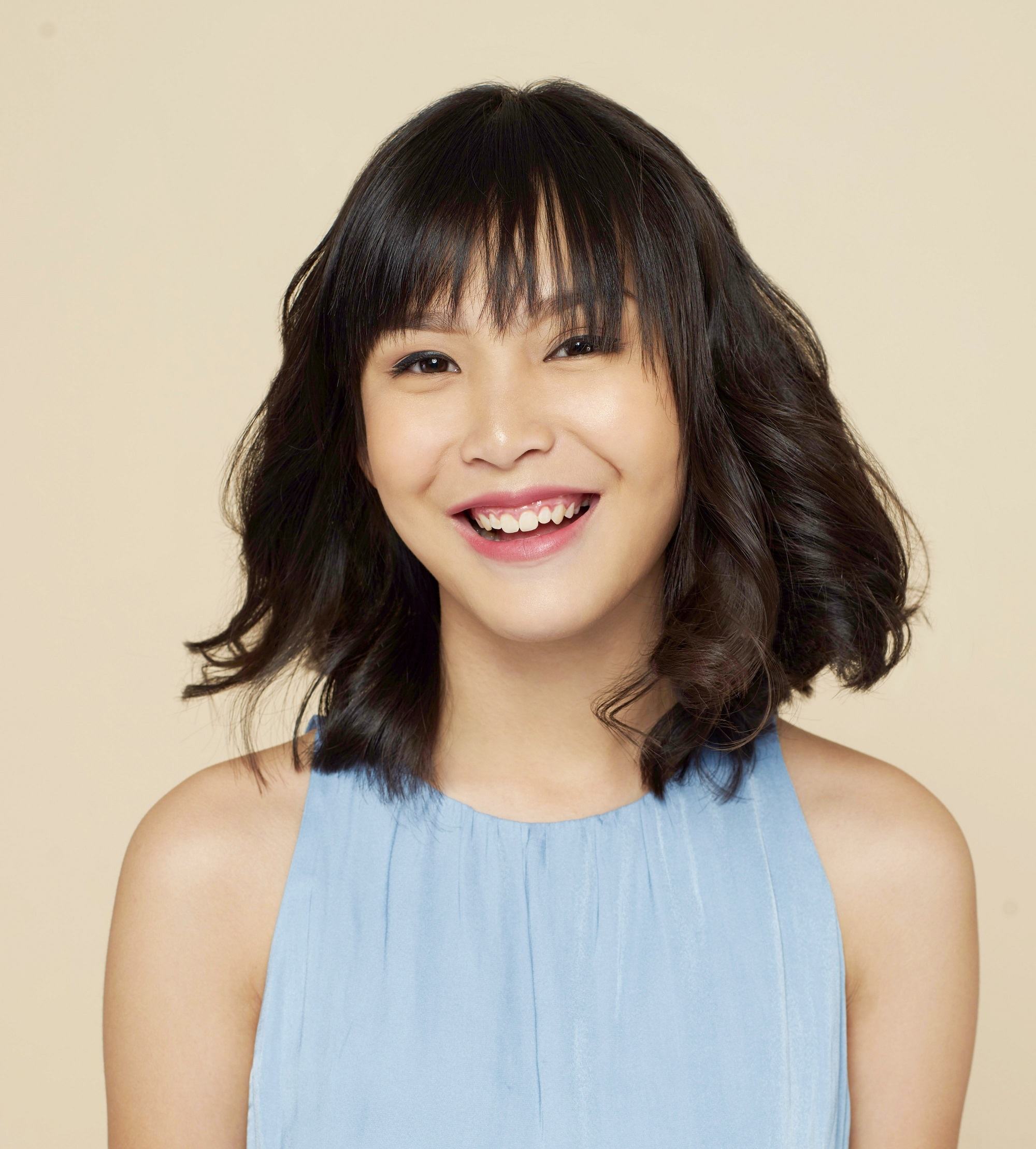 New Year's Eve hairstyles: Closeup shot of an Asian woman with curly long bob wearing a blue sleeveless dress
