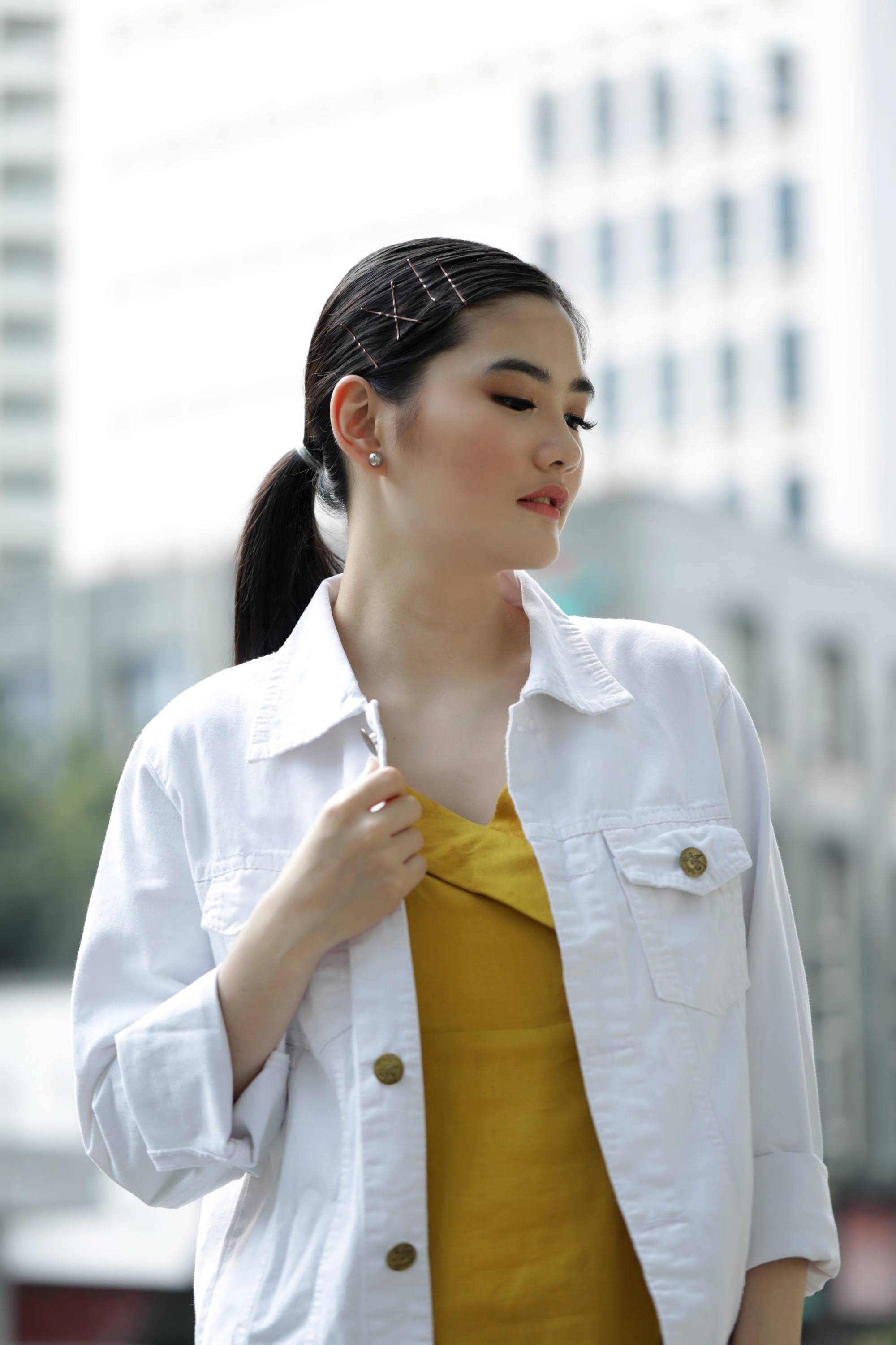 New Year's Eve Hairstyles: Asian woman with long hair in a ponytail wearing a white jacket and mustard-colored dress