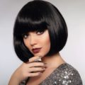 Should I get bangs: Closeup shot of a woman with black bob and blunt bangs wearing a sparkly dress