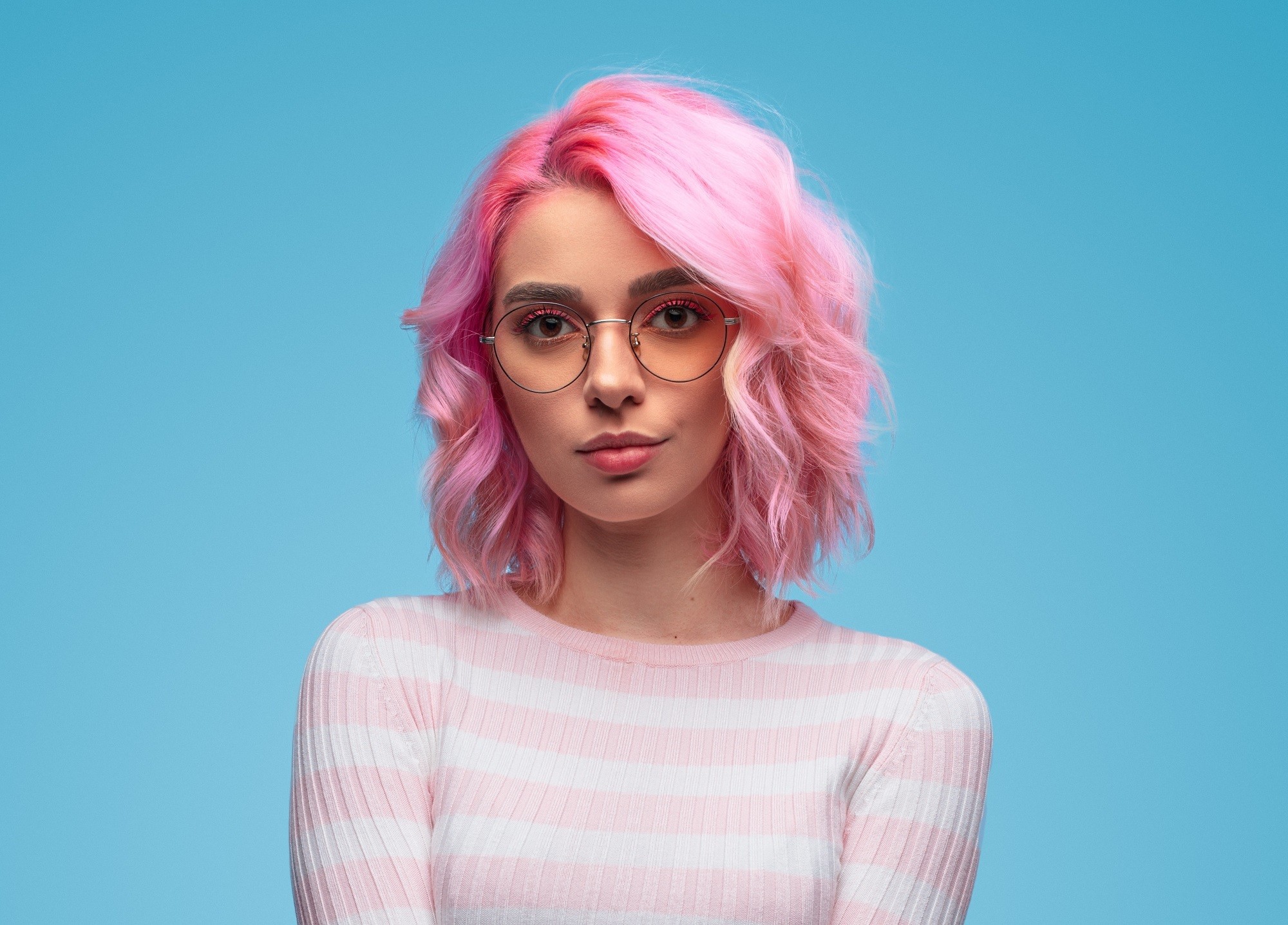 Bob ondulé : gros plan d'une fille avec un bob rose ondulé portant des lunettes et des manches longues à rayures blanches et roses