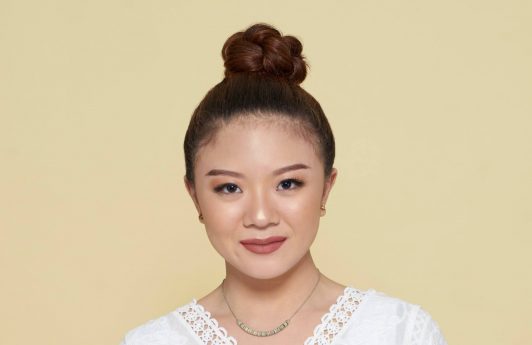 How to style curly hair: Asian woman with curly hair in a top knot smiling