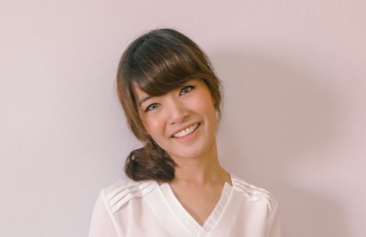 Medium length haircuts with bangs: Closeup shot of a woman with dark brown medium hair with bangs in a side ponytail wearing a white blouse