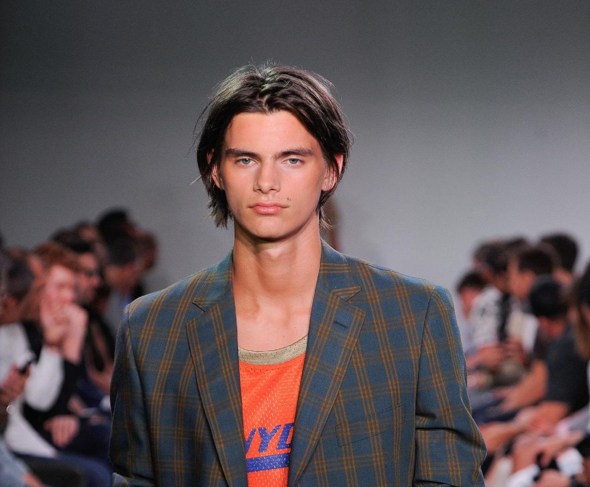 New hairstyles for men: Man with dark brown medium hair wearing a suit at a runway show