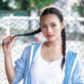 Simple braids and film festival hairstyles: Asian woman wearing a blue jacket with long black hair in boxer braid standing against a fence