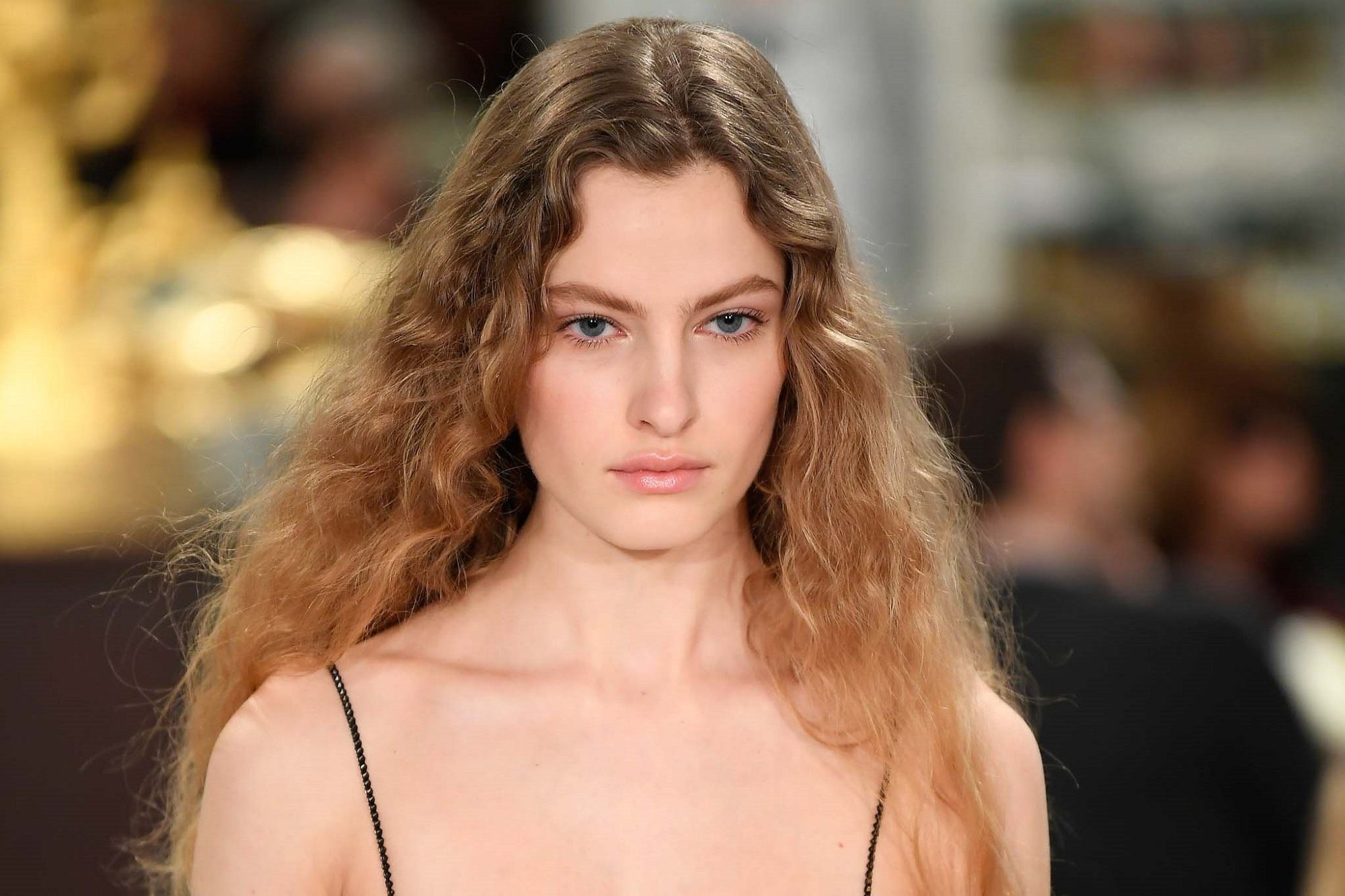 New York Fashion Week Hair: Closeup shot of a woman with long brown curly hair wearing a thin-strapped dress