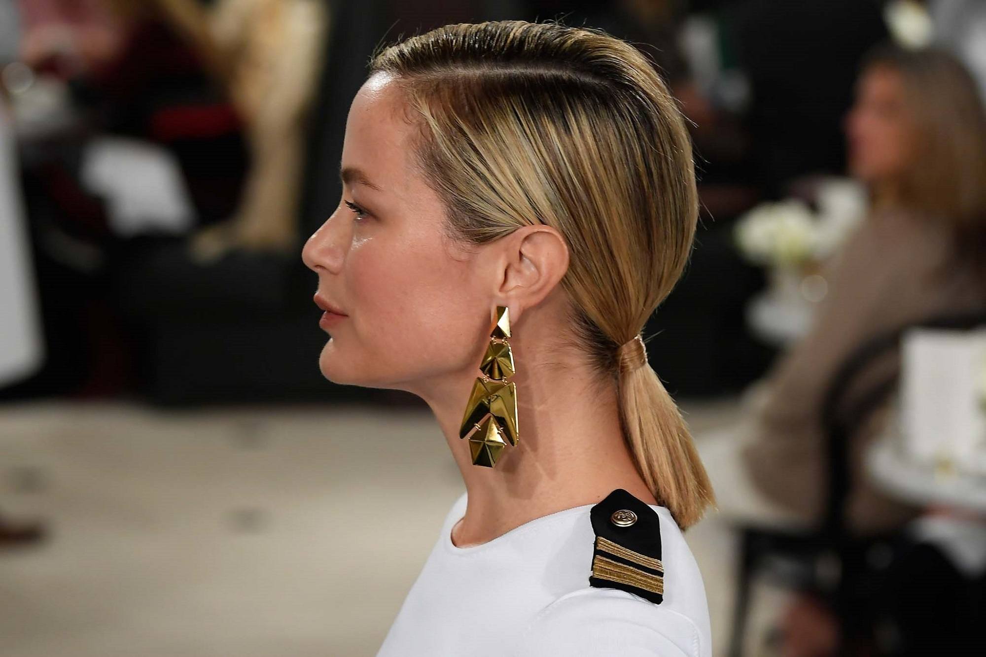 New York Fashion Week Hair: Side view shot of a woman with straight blonde hair in a ponytail wearing big earrings and white top