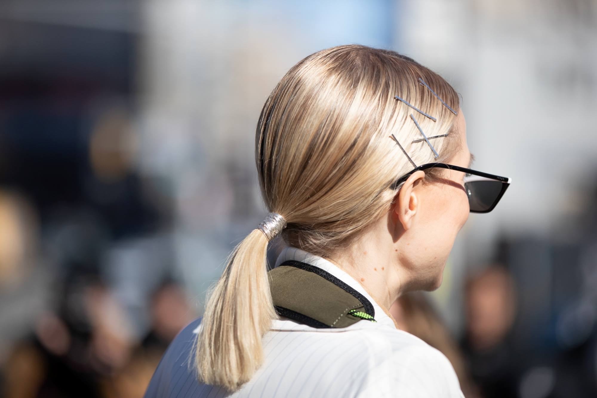Street style hair inspiration: Back shot of a woman with shoulder length blonde hair in a ponytail outdoors