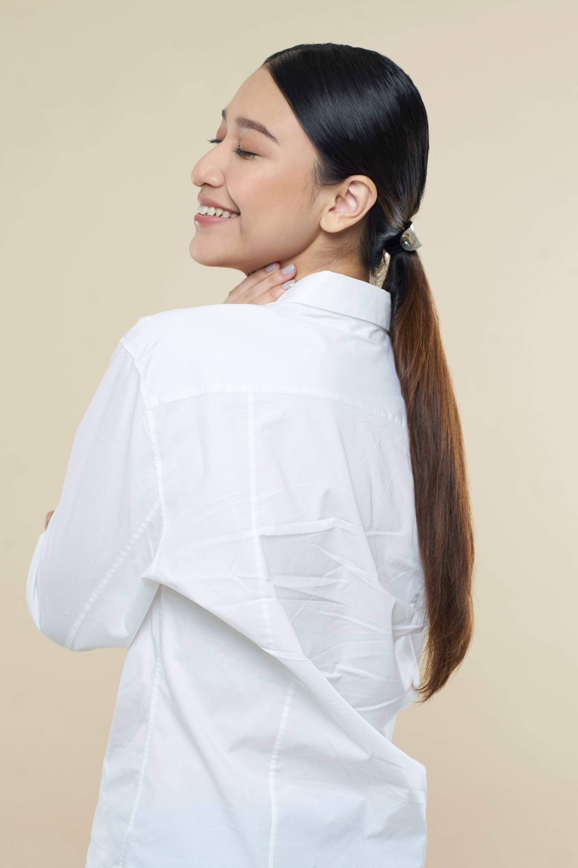 Sleek tied hair: Side view of an Asian woman with long dark hair in low ponytail wearing a white blouse