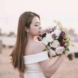 Asian woman showing her bridal hairstyle while standing on a beach holding flowers