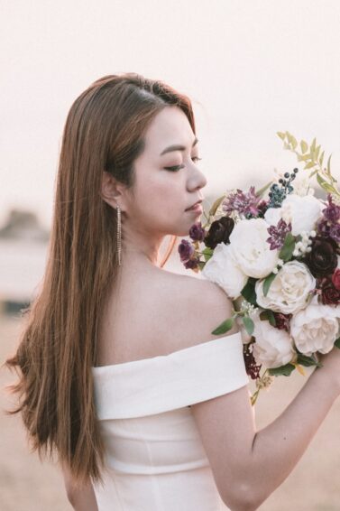 Asian woman showing her bridal hairstyle while standing on a beach holding flowers