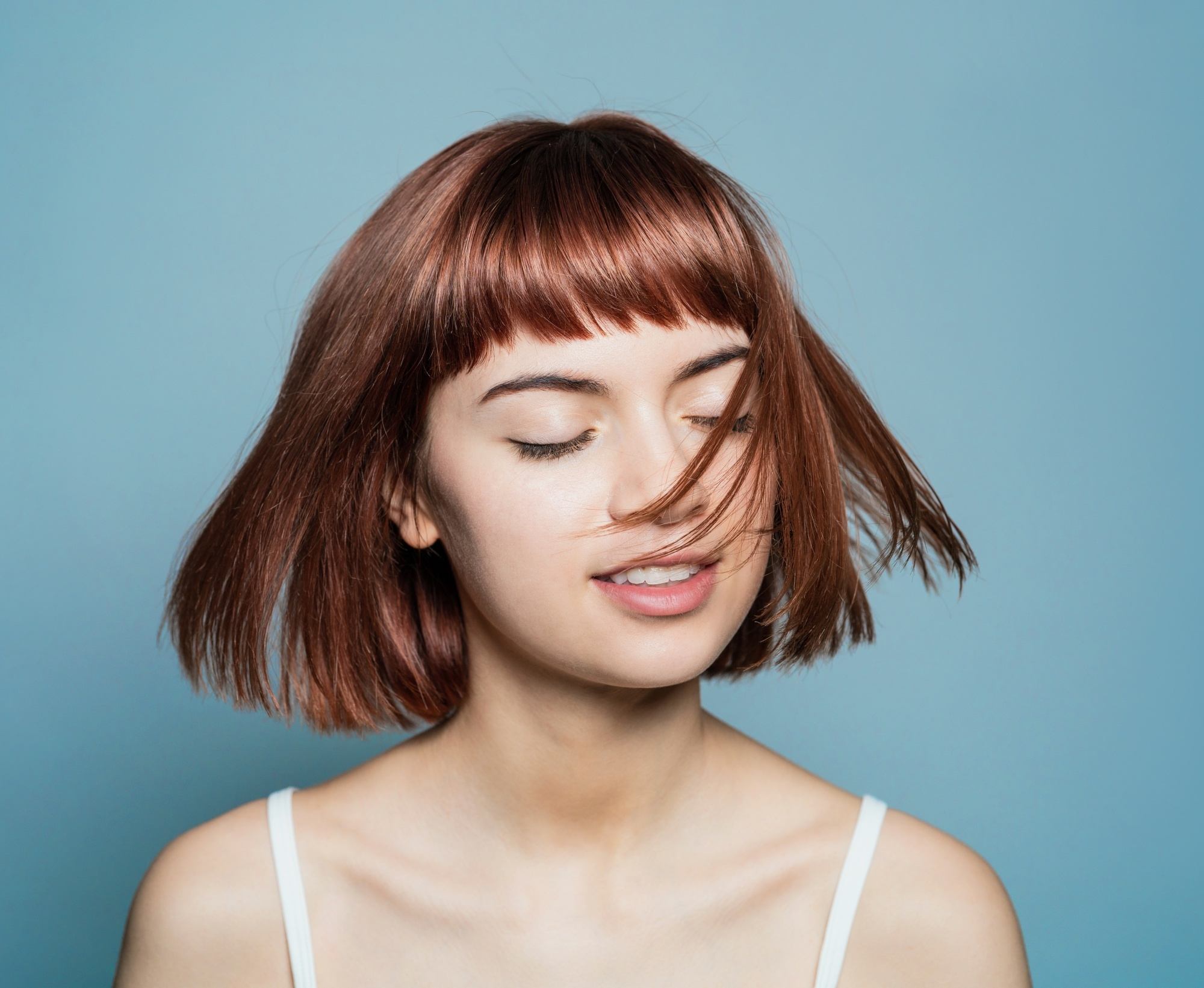 Bob haircuts for fine hair: Closeup shot of a woman with straight short brown hair with bangs with eyes closed
