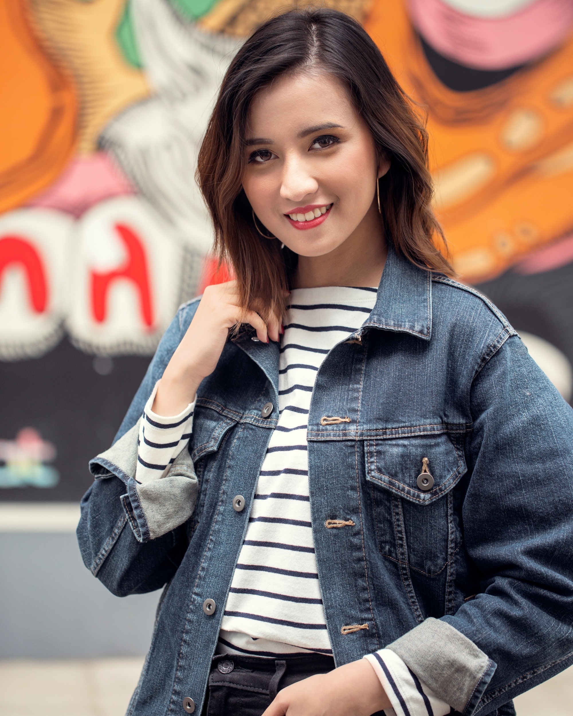 Bob haircuts for fine hair: Asian woman with dark brown messy layered bob wearing a denim jacket in front of a street mural