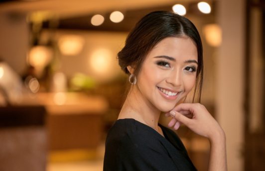 Chignon for short hair: Asian woman with dark hair in a chignon smiling in a hotel lobby
