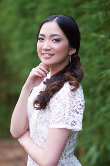 Curly hair prom: Asian woman with long dark hair in a curly side ponytail wearing a white dress outdoors