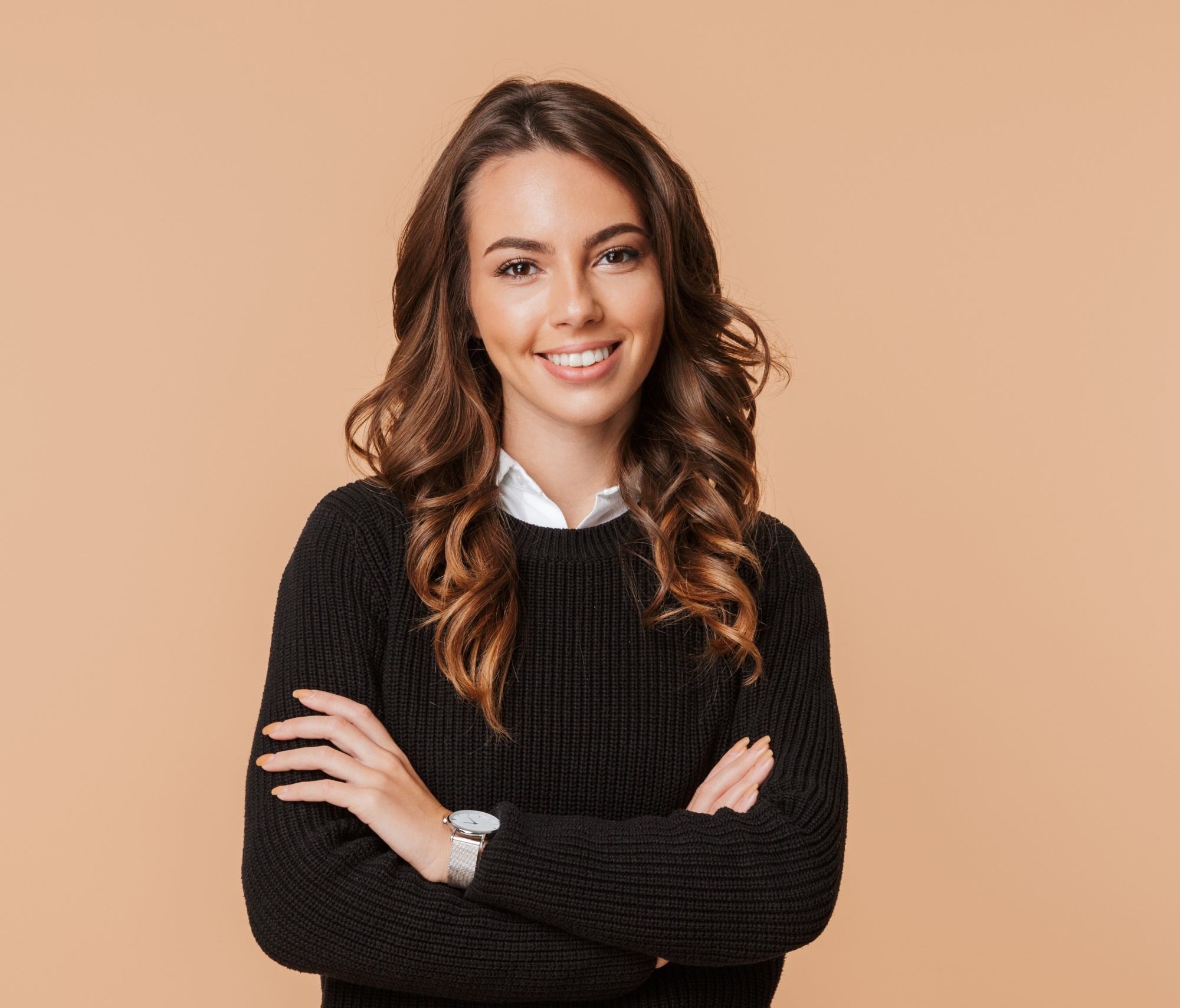 Golden brown hair color: Woman with long wavy brown hair wearing a black shirt against a peach backdrop